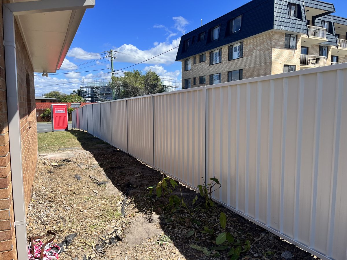 Long cream Colorbond boundary fence beside a brick house