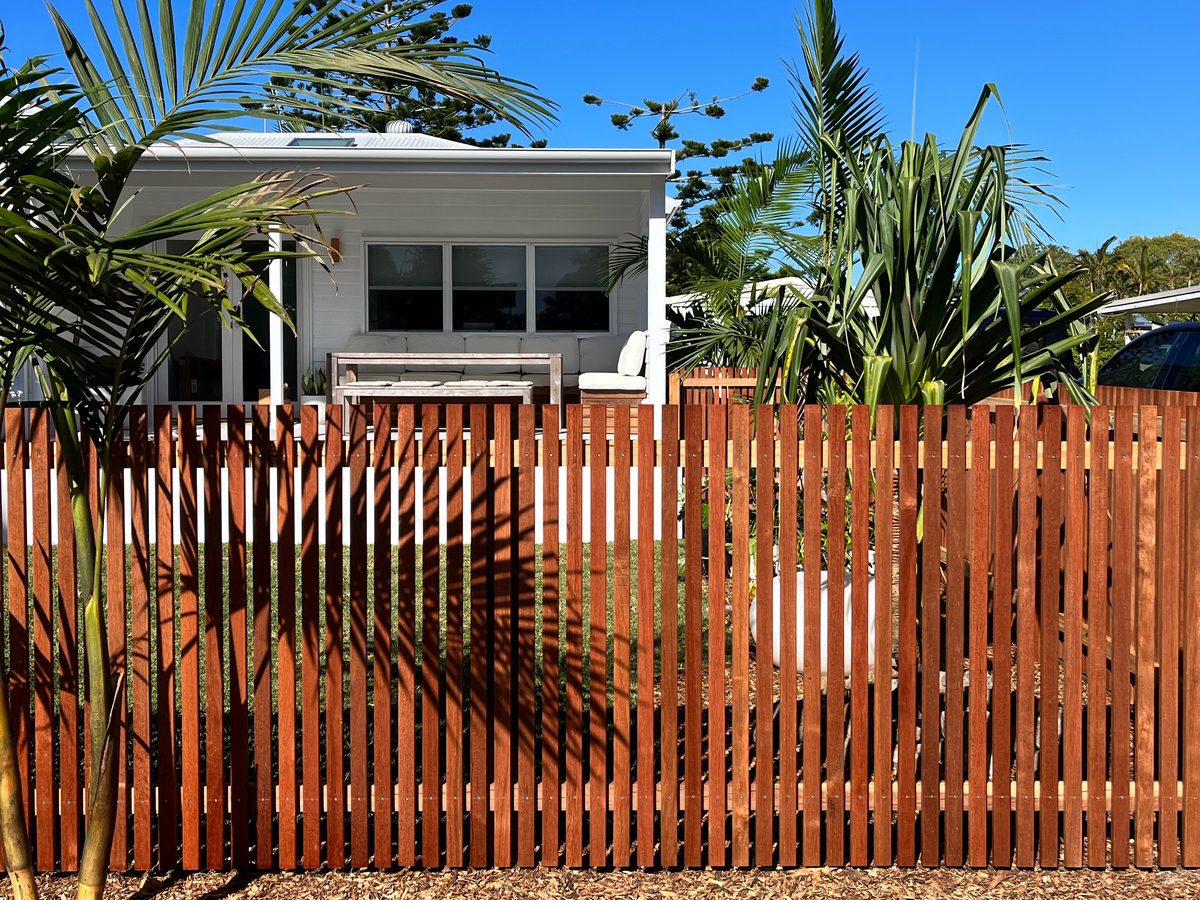 Hardwood vertical slat fence in front of a white cottage with palm trees